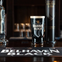 An advertising image showing a pint of Belhaven Black sat on a wooden bar top.