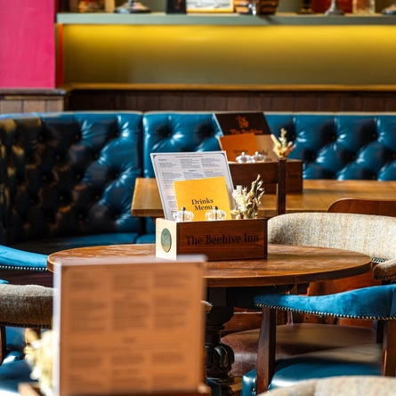 A close up view of restaurant tables inside The Beehive Inn, with upholstered chairs and a booth seat.