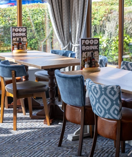 A close up view of two restaurant tables with upholstered chairs, in the conservatory area inside The Wall's End.