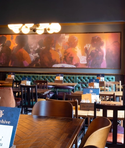 An interior restaurant seating area at The Beehive Inn, with an upholstered booth seat, and framed artwork on the green wallpapered walls.