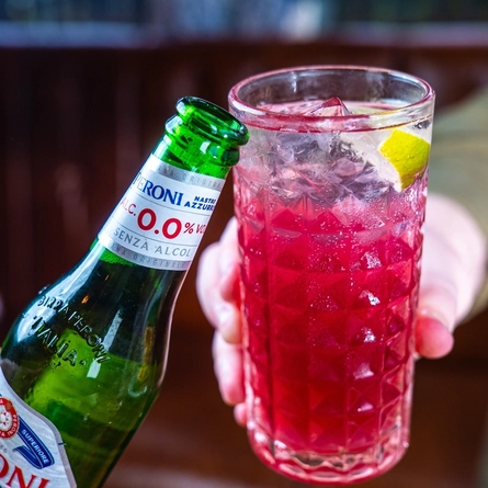 Two hands clink together a bottle of Peroni low alcohol beer and another drink in a glass.