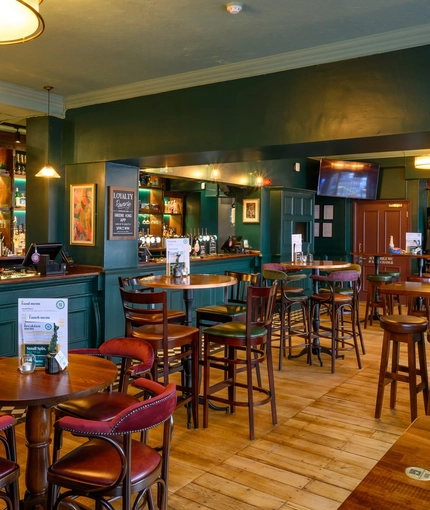 The ground floor bar and interior restaurant seating area at The Globe; with checkerboard tiles in front of the counter, TVs on the walls, two gaming machines, and bar stool seating.
