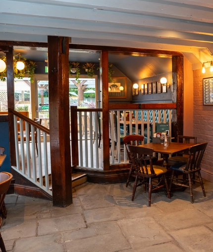 An interior restaurant seating area at the Tredegar Arms, with wooden beams, a paved stone floor, and a few steps leading up to another seating area.