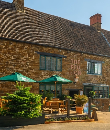 The beer garden with picnic benches and parasols at The Red Lion, Adderbury.