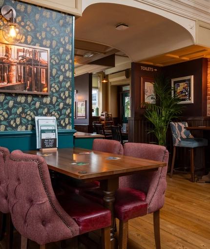 An interior restaurant seating area at The White Lion in Frenchay, with wooden tables, upholstered chairs, and framed artwork on the walls.