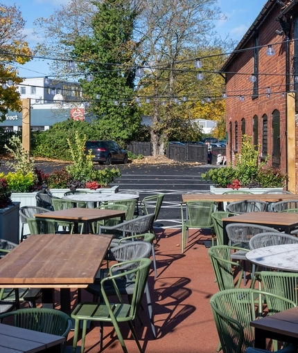 The exterior beer garden seating area at The Fox in Bury St Edmunds, with plants in raised planter boxes, and string lights above the tables and chairs.