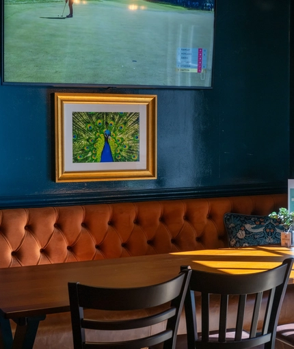 The interior restaurant seating area of the Cock & Pye, with upholstered booth seating and a TV on the wall.