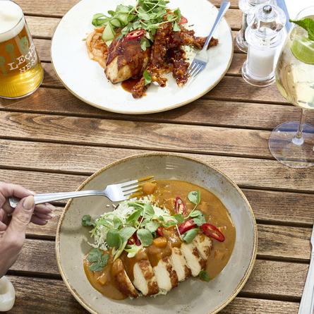 A lifestyle image showing a person sat at a table within the exterior beer garden seating area enjoying a main dish and drinks at a Chef & Brewer venue.
