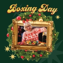 A banner showing the words "Boxing Day" in golden letters, above a Christmas wreath containing an image of a person sitting at a restaurant table with a plate of roast dinner in front of them and pouring custard over a plate of pudding. The text and image sit on a dark green background and are surrounded by gold stars.