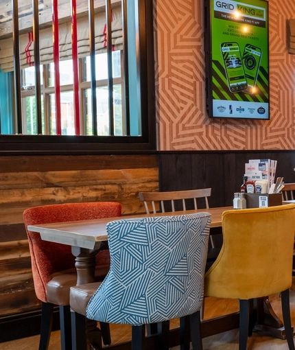 The interior restaurant seating area at the Arch & Anchor, with wooden tables, upholstered seats, and TVs on the walls.