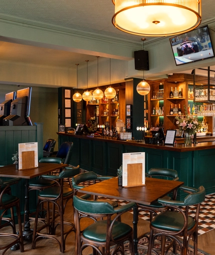 The bar and interior restaurant seating area at The Richmond Arms, with a TV on the wall, bar stool seating, and gaming machines.