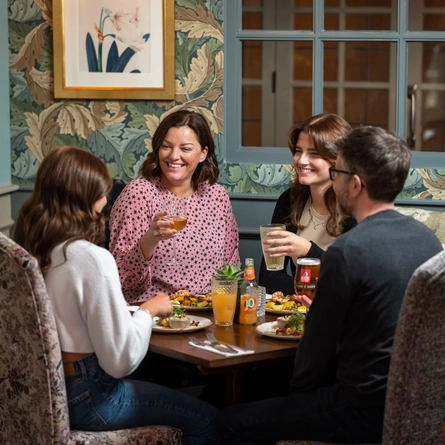 A group of people sitting around a table smiling and having a meal, with drinks in their hands.