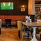 The interior restaurant seating area at the Arch & Anchor, with wooden tables, upholstered seats, and TVs on the walls.