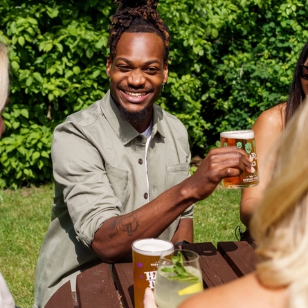 A mixed group of people, sitting at an outdoor table, enjoying a variety of drinks and conversation.