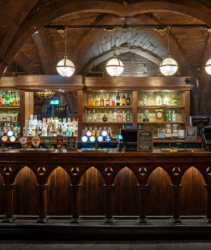 An image showing the interior bar area with wooden gothic arched carvings and stone vaulted ceiling at The Watergates Bar.