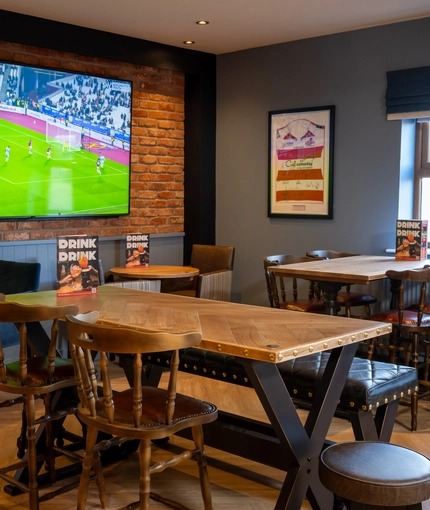 The interior restaurant seating area of The Parsonage in Leigh, with wooden tables and a TV on the wall.