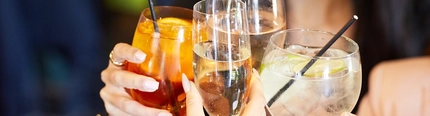 A close up view of two cocktails, a glass of champagne, and a glass of wine, being clinked together.