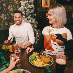 Four people sitting at a restaurant table with plates of food in front of them. One person is holding a glass of Level Head IPA, another person is holding a glass of champagne, and a cocktail and a glass of Guinness sit on the table.