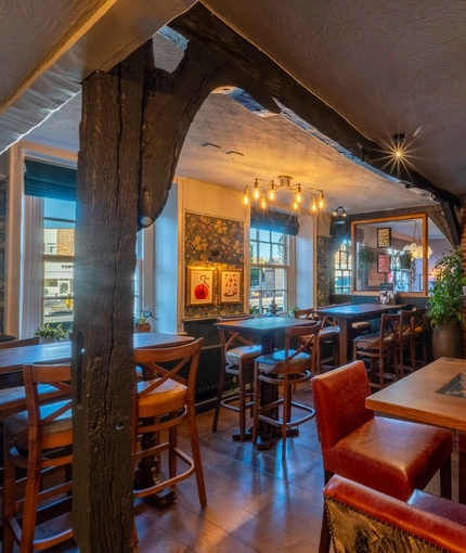The interior restaurant seating area of The White Hart in Frimley, with wooden beams, and a TV on the wall.