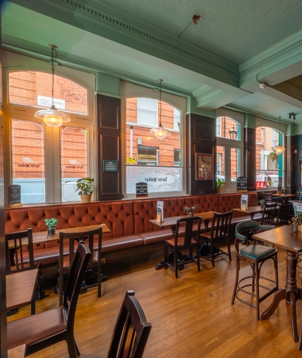 An interior restaurant seating area at The Plough, with a long, upholstered booth seat below the windows.