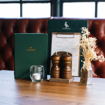 A close up view of menus, salt and pepper mills, a tea light, and a table ornament, on a restaurant table inside Ye Olde Swan.
