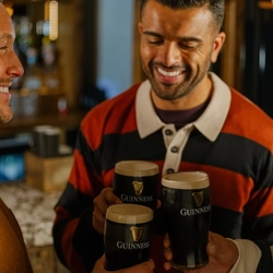 An image focusing on 2 friends stood within a group of friends celebrating St Patricks Day with a cheers with pints of Guinness stood within the interior at The Crown.