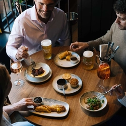 A lifestyle image showing 4 people sat at a table within the interior restaurant seating area enjoying a selection of drinks and bar snack dishes at a Heritage venue.