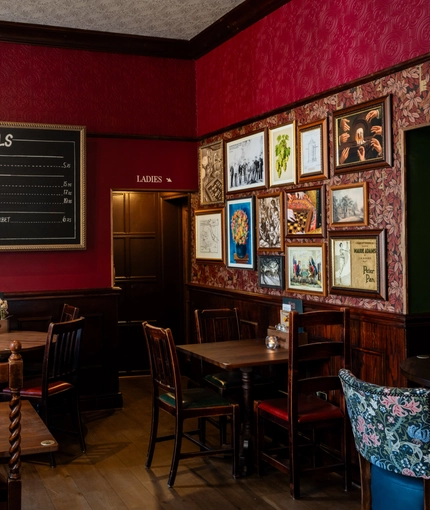 An interior restaurant seating area at the King's Head, with dark wood floors; textured red wallpaper; and framed artwork on the wall.