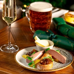 A festive decorated wooden table holding a plated Pate starter and a glass of sparkling wine and a tankard of beer.