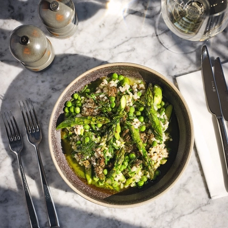 An overhead advertising image of a bowled Risotto & Parmesan dish and glass of white wine sat on an interior table at The White Horses.