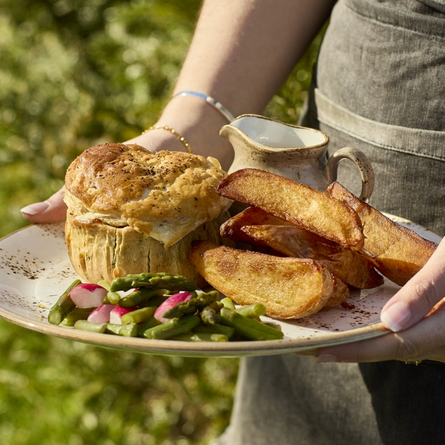 Hands holding a plate of pie, potato wedges and vegetables.
