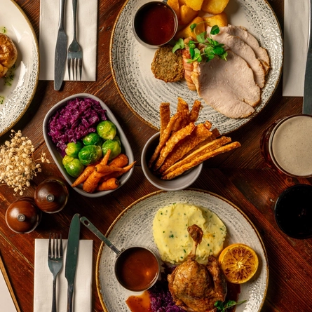 An overhead shot of a range of plated meals on a festive decorated wooden table.
