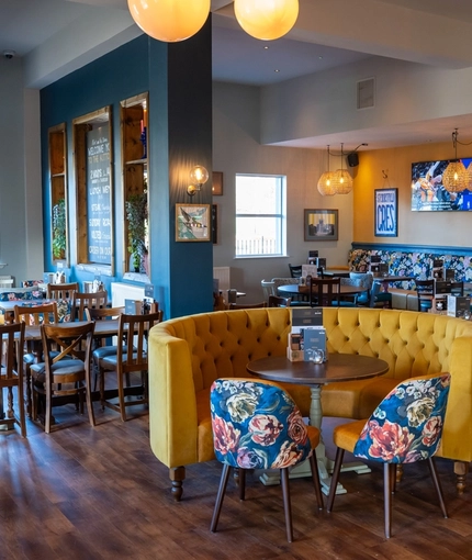 The interior restaurant seating area of The Kittoch in East Kilbride, with upholstered booth seats, and framed artwork and a TV on the wall.