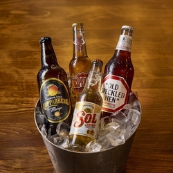 Bottles of Koppaberg cider, Sol, Desperados, and Old Speckled Hen sitting in a bucket of ice.