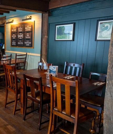 An interior restaurant seating area at The Rising Sun in Wistaston, with wood panelled walls, wooden beams on the walls and ceiling, and a brick fireplace.