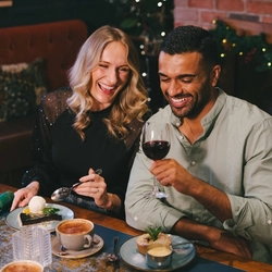 An image focusing on 2 people sat with friends enjoying various dessert dishes and a selection of drinks while sat within the interior restaurant seating area.
