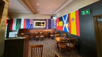 An image of an interior seating area with tables, chairs and various flags hanging on the walls to celebrate The World Cup.