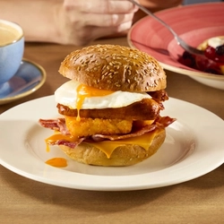 The Big Brekkie Roll at Hungry Horse venues, featuring fried egg, sausage, hash brown and cheese, served on a plate. The plate sits on a table next to a cup of coffee and a bowl containing a waffle topped with berries and cream.