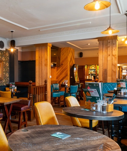 The interior restaurant seating area at The Talbot in Worcester; with upholstered chairs, benches, and booth seating; a TV on the wall; and a gaming machine.