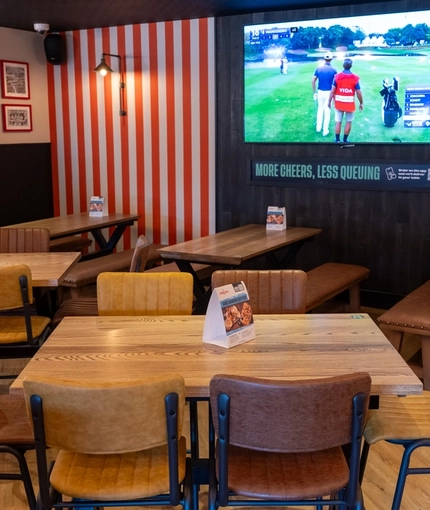 An interior restaurant seating area at The Lodge in Alvaston, with upholstered bench seats, dartboards, and a large TV on the wall.