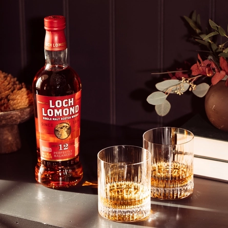 A bottle of Loch Lomond 12YO Whisky on a table with two whisky glasses containing whisky.