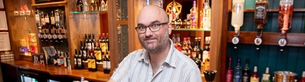 A man, standing behind a bar and pulling a pint.