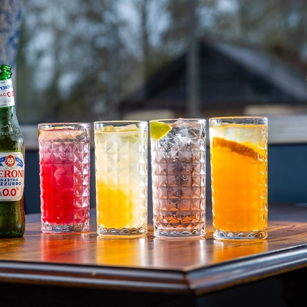 Bottles of Heineken and Peroni low alcohol beer on a table next to glasses of other drinks.