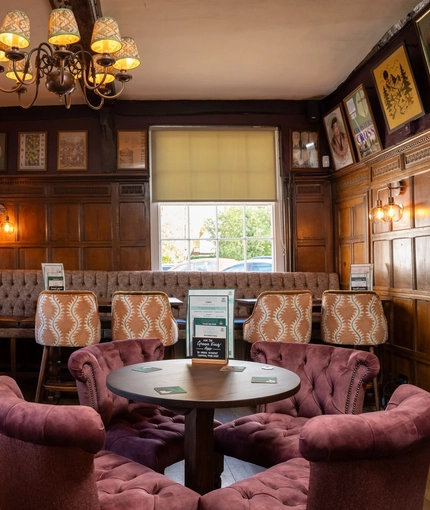 The wood panelled interior restaurant seating area at The Fox, with upholstered chairs, and framed artwork on the walls.