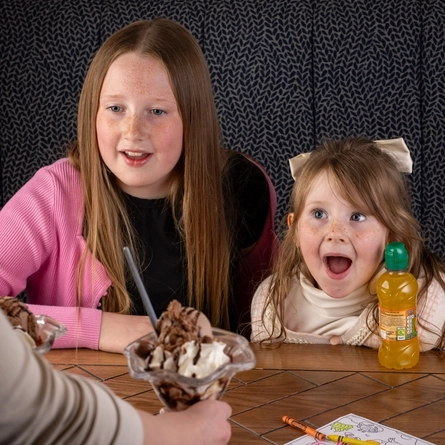 Two children looking excited being served an ice-cream sundae at a Flaming Grill venue.