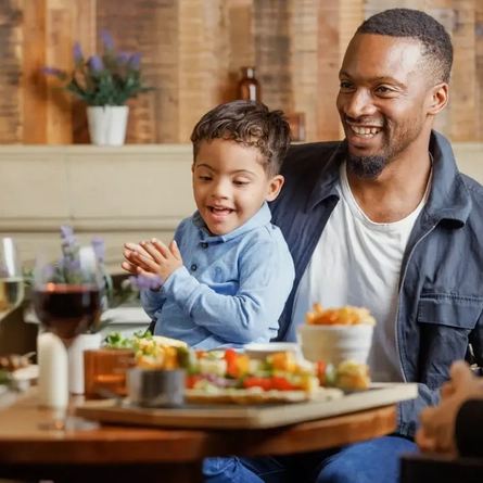 A child on his father's lap at a table full of food