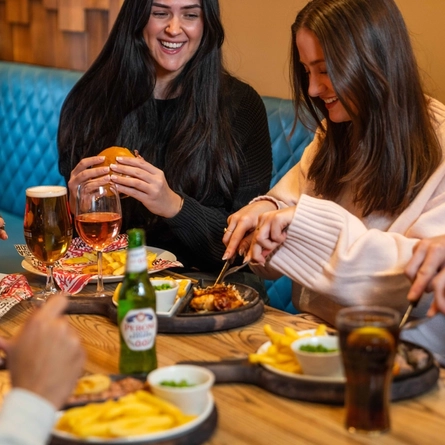 An image showing a group of people sat around a table enjoying mains dishes and drinks at a Flaming Grill venue.