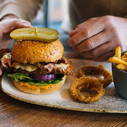 A close up image of a person sat at a table within the interior restaurant seating area enjoying a pint of Hazy Day and a Burger dish at a Heritage venue.