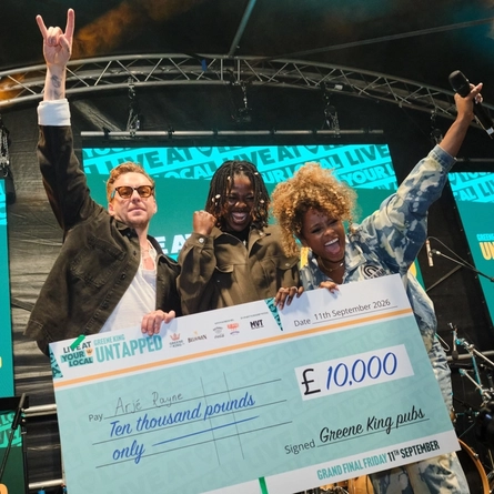 The winner of the Greene King Live At Your Local 2026 competition, Arjé Rayne, celebrating on stage with judges Danny Jones and Fleur East as they hold a giant cheque for the £10,000 prize.