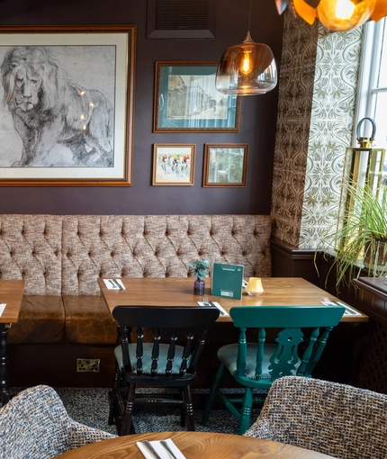 An interior restaurant booth seating area at The White Lion, with upholstered seat, and framed artwork on the wall.